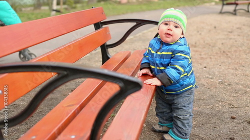 Happy baby is standing next to the bench on the playground 
 photo