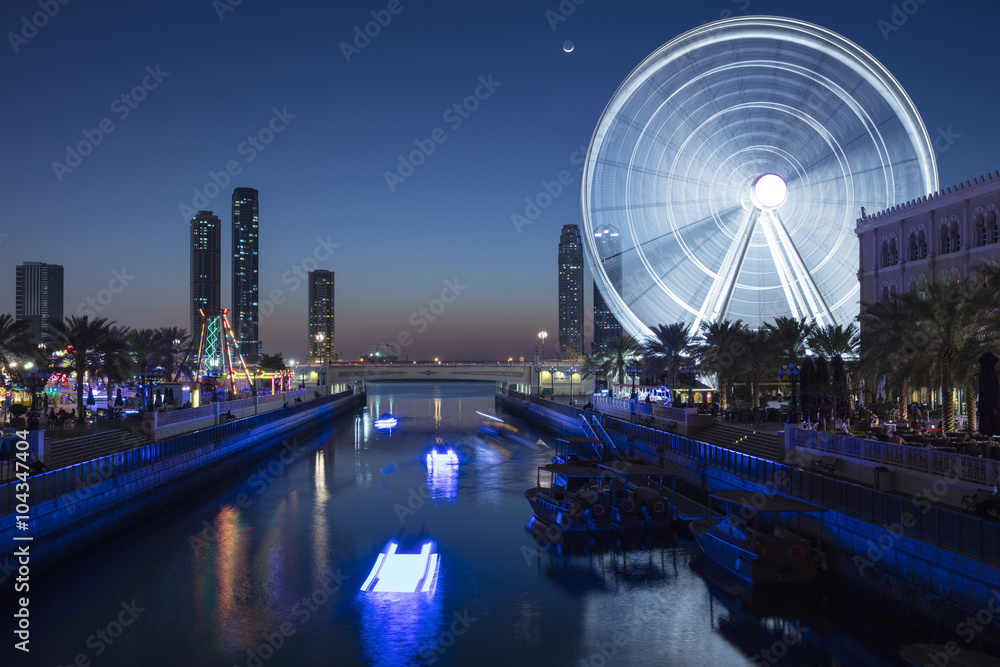 water channel with reflection and night light of ferris wheel in emirates city