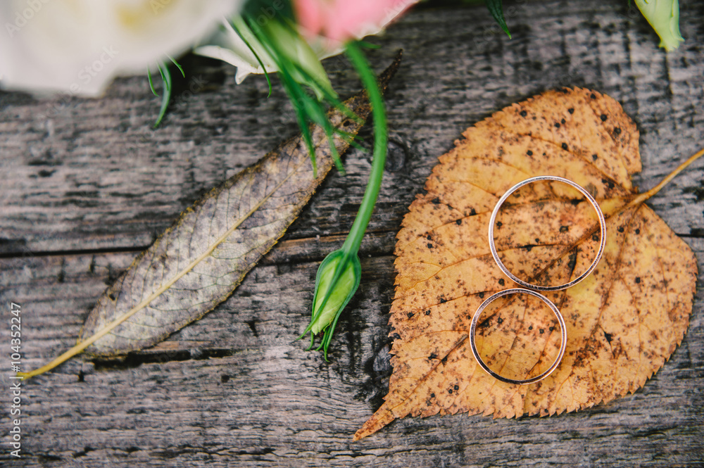 Gold wedding rings on orange/autumn leave and wooden texture background. Wedding card, wedding background. Gold wedding rings on orange/autumn leave and wooden texture background. Wedding card, wedding background.