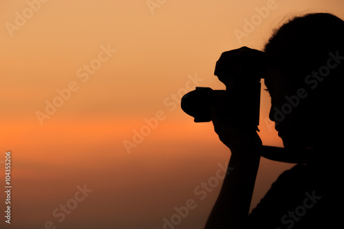 Silhouette of woman shooting with camera at sunset