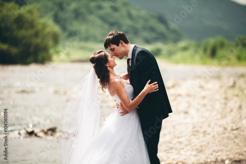 Elegant gentle stylish groom and bride near river with stones. Wedding couple in love © olegparylyak
