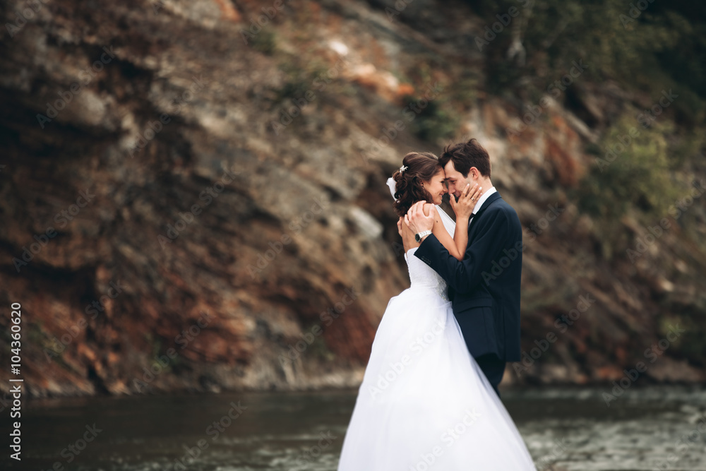 Elegant gentle stylish groom and bride near river with stones. Wedding couple in love Elegant gentle stylish groom and bride near river with stones. Wedding couple in love