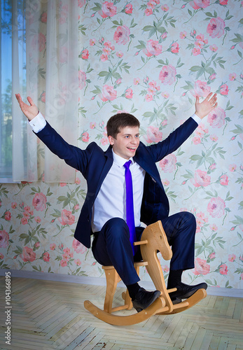 Obraz na plátně Happy childish young man in business suit riding toy wooden horse
