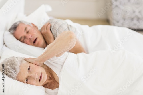 Awake senior woman in bed covering her ears