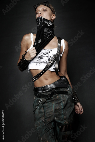 Young woman in brutal style clothes with goggles on studio black background