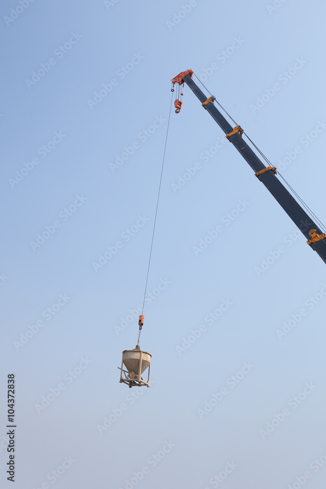 Crane lifting concrete mixer container against sky Crane lifting concrete mixer container against sky