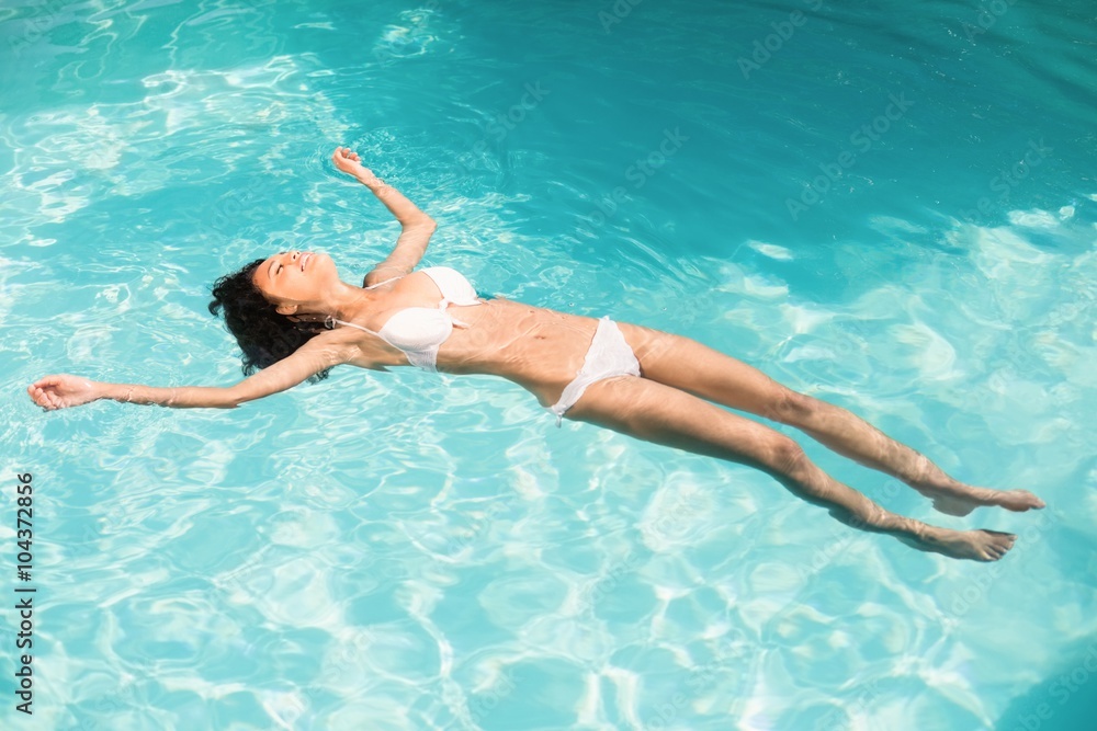 Beautiful woman in white bikini floating in swimming pool
