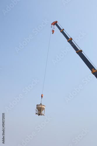 Crane lifting concrete mixer container against sky