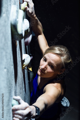 Fit woman rock climbing indoors at the gym.