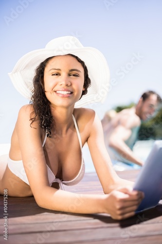 Portrait of happy woman in hat using digital tablet by pool side