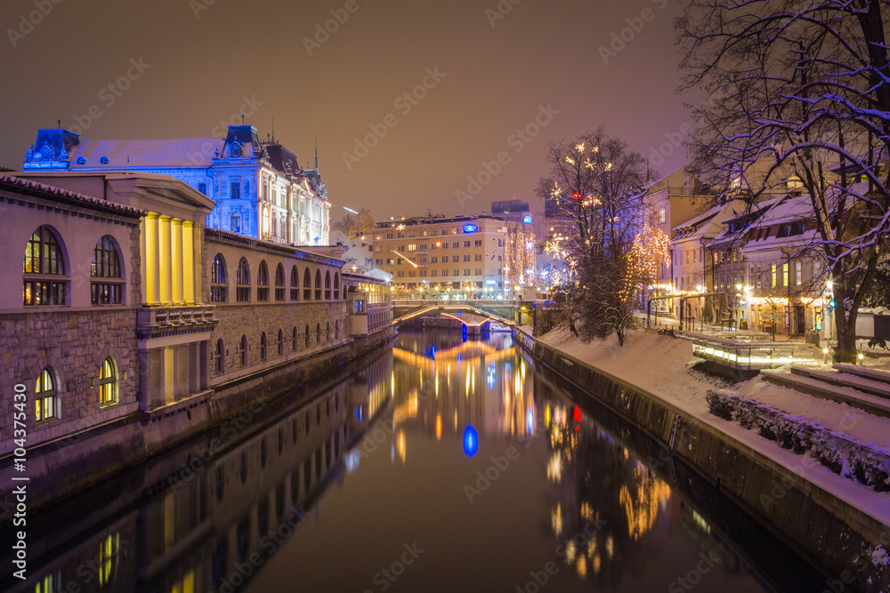 Night view of Ljubljanica river with snowy banks and festive lights during christmas eve, Ljubljana, Slovenia.