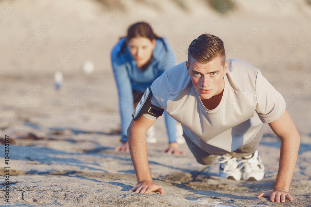 Fototapeta premium Young couple doing push ups on ocean beach