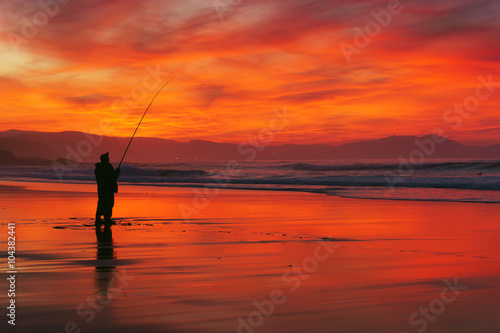 fisherman silhouette on beach at sunset