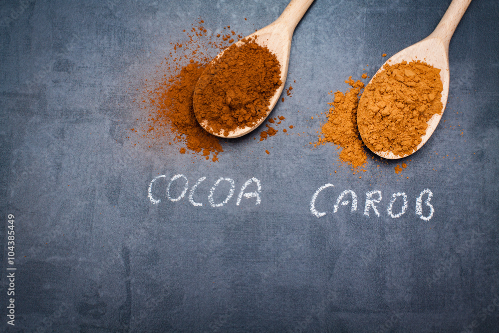Cocoa and carob powder on wooden spoons chalk signed on blck stone background.