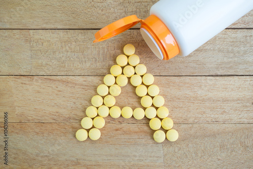 Yellow pills forming shape to A alphabet on wood background photo