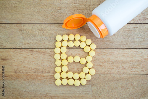 Yellow pills forming shape to B alphabet on wood background