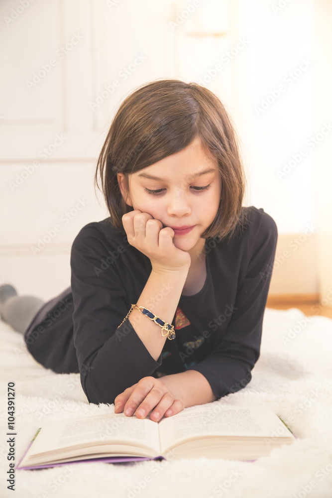 Portrait of girl lying on blanket on the floor reading a book Stock
