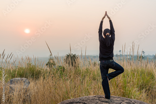 Woman practicing yoga on the top rock at sunset.