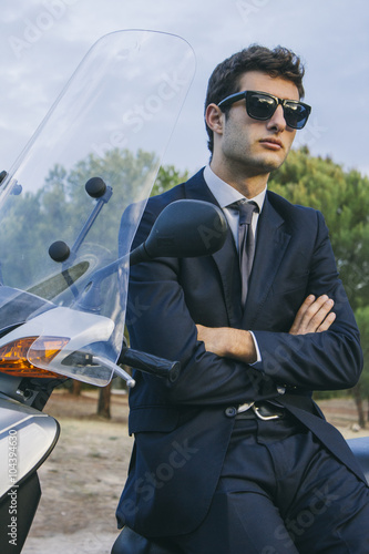 Portrait of young businessman wearing sunglasses sitting on motor scooter photo