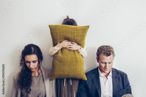 Couple having relationship conflict with their daughter hiding her face behind cushion photo