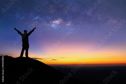 Silhouette of man is standing on top of mountain and spreading hand to the sky