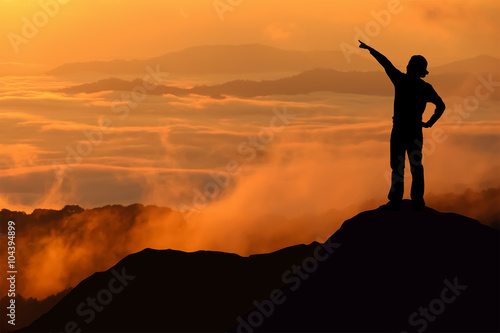 Silhouette of tourist woman standing and pointing on top of a mountain.