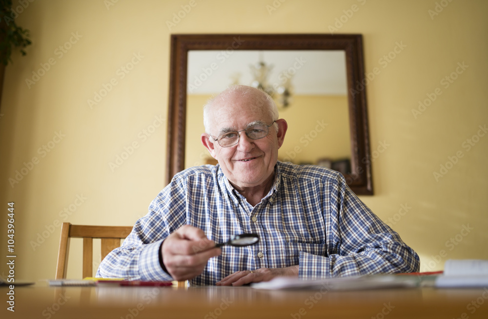 Portrait of smiling senior man with magnifier sitting at a table Portrait of smiling senior man with magnifier sitting at a table