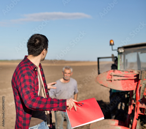 Farmer with worker and tractor on field