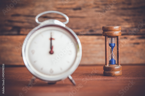 Retro alarm clock and hourglass on table with wooden background,vintage color tone
