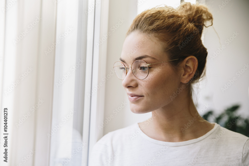 Young woman with eyeglasses looking out of her window Young woman with eyeglasses looking out of her window
