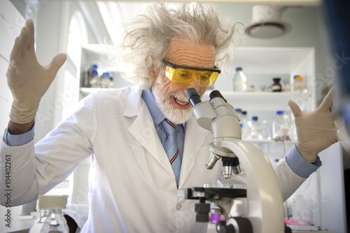 Tousled professor examining samples under microscope, looking surprised photo