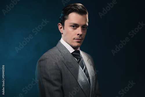 Fotografia Retro 1940s business man in suit and tie against blue wall.