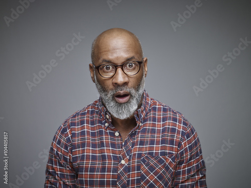 Portrait of astonished man wearing spectacles and checked shirt in front of grey background