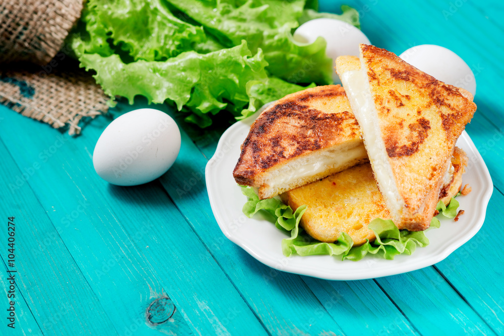 
sandwich with cheese and mayonnaise fried in egg with lettuce on a wooden background