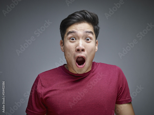 Portrait of shocked young man in front of grey background