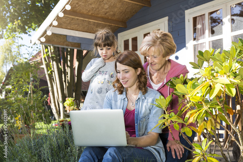 Grandmother, mother and daughter looking at laptop on garden terrace photo