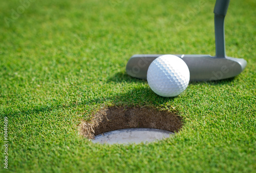 Close-up of golf hole with putter and ball photo