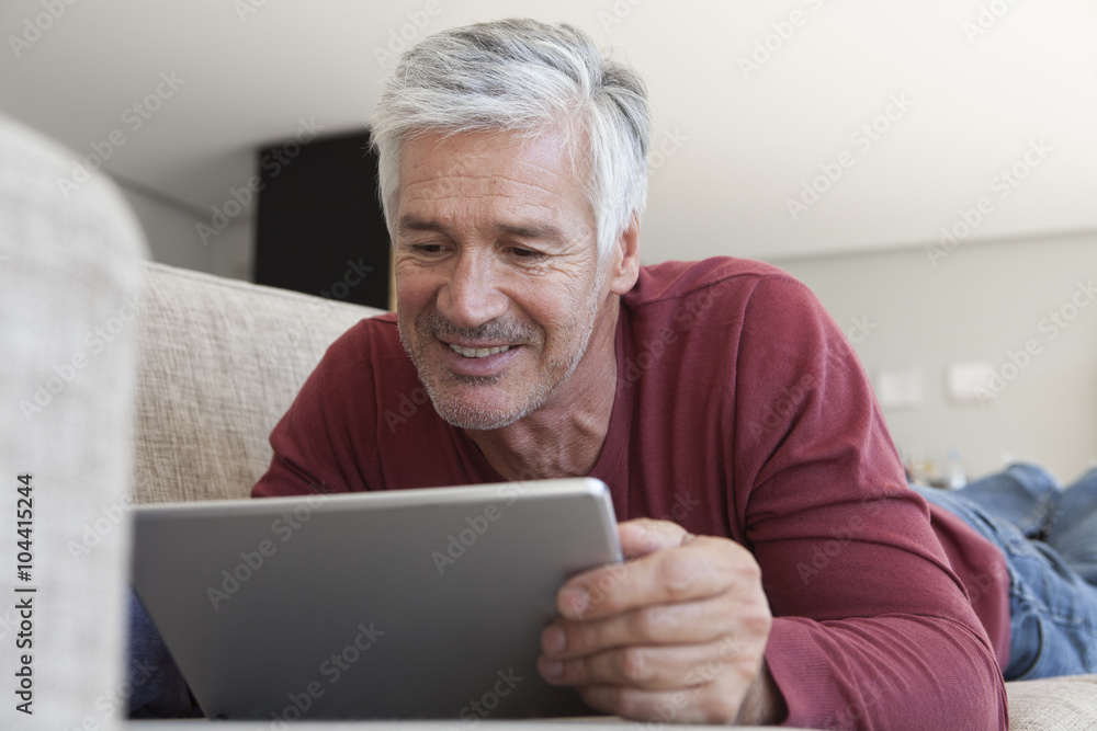 Portrait of smiling man lying on the couch at home using digital tablet Portrait of smiling man lying on the couch at home using digital tablet