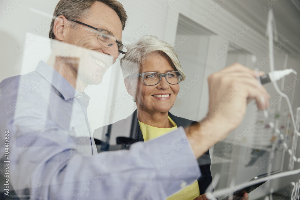 Man writing onto glass wall in office Man writing onto glass wall in office
