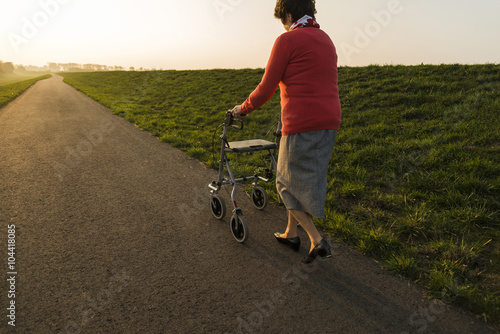 Senior woman walking with wheeled walker on a path