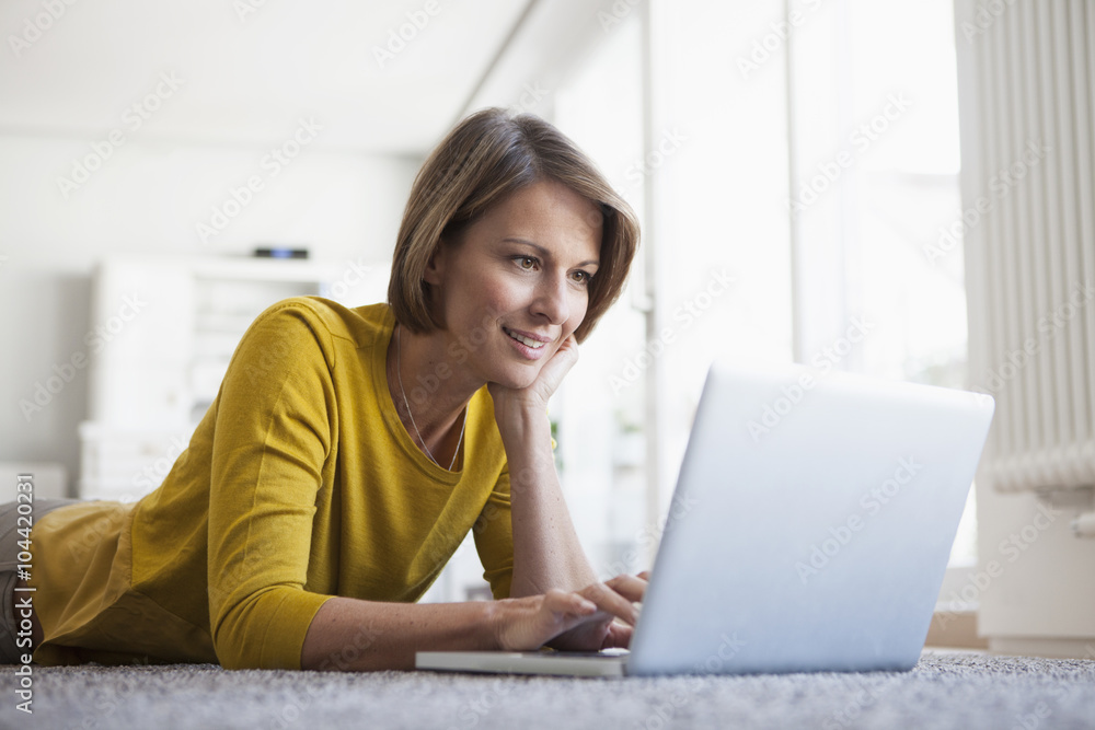 Relaxed woman at home lying on floor using laptop Relaxed woman at home lying on floor using laptop