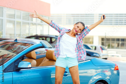 Young emotional woman standing near a convertible with the keys