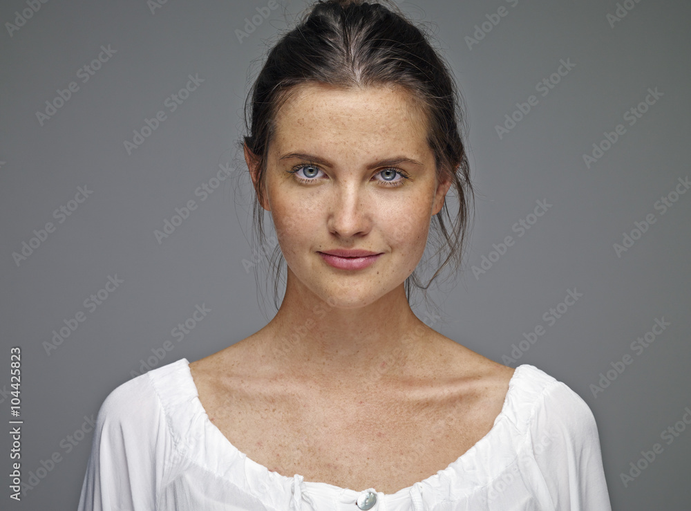 Portrait of young woman with brown hair and blue eyes in front of grey background Portrait of young woman with brown hair and blue eyes in front of grey background
