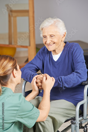 Seniorin im Rollstuhl hält Hände mit Krankenpflegerin