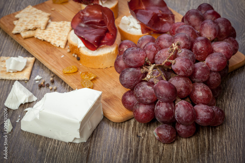 White cheese, ham, crackers and grape on wooden background
