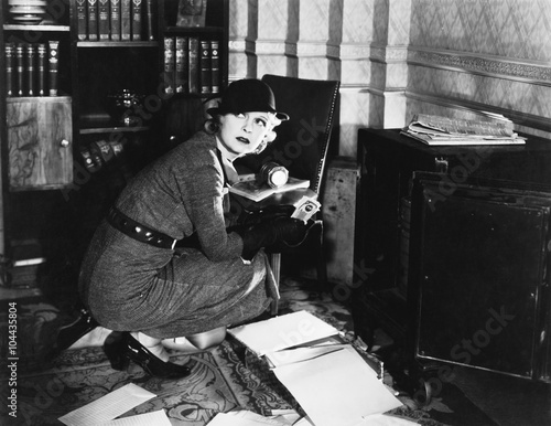 Canvas Print Young woman in an office next to a safe, looking over her shoulder