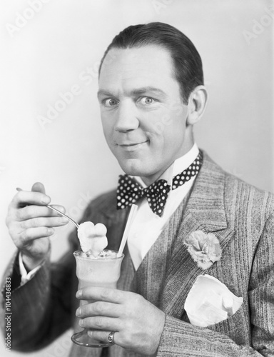 Man eating an icecream out of a glass with a straw 