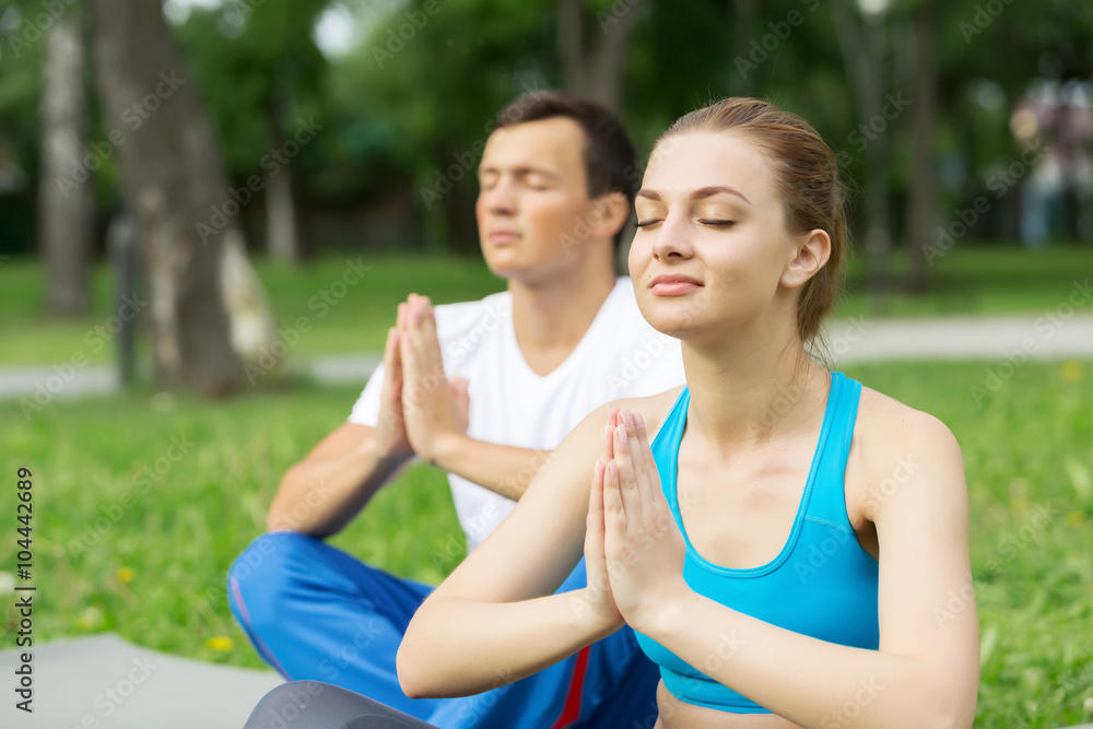 Fototapeta premium Young couple meditating on green grass