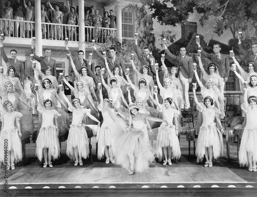Group of dancers standing on a stage with their arms in the air and a drink in their hands 