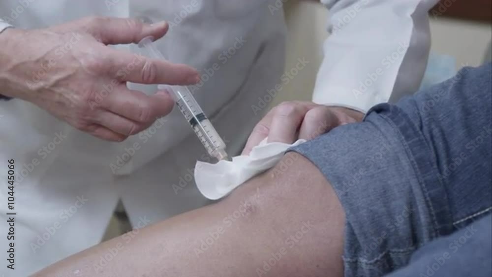 Tight shot of doctor making injection to patient's knee. Tight shot of doctor making injection to patient's knee.